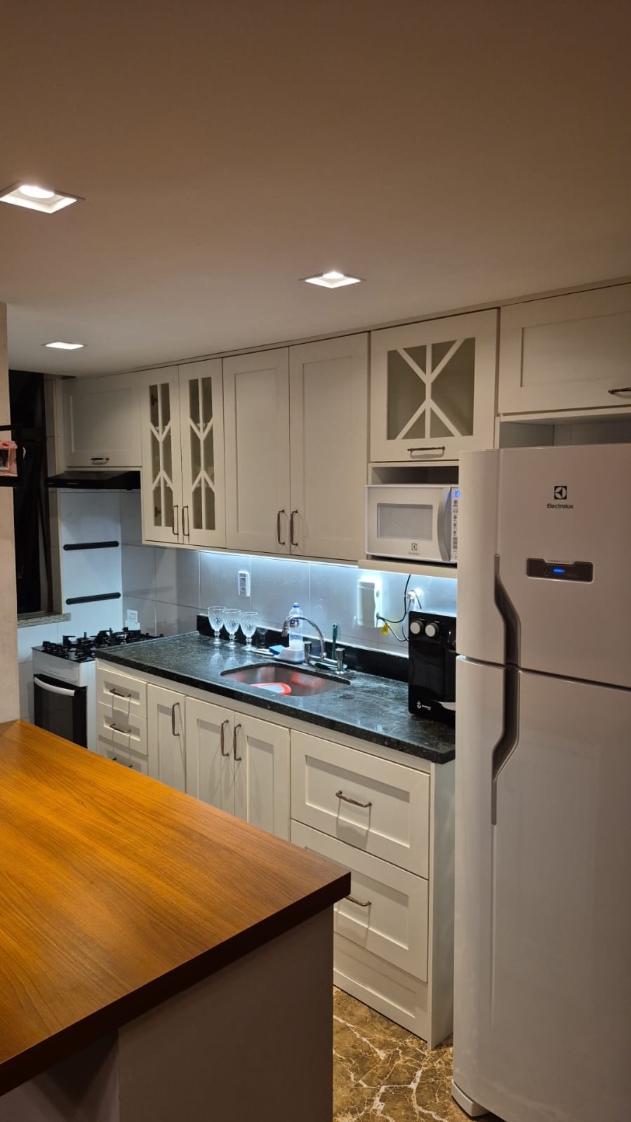 Cozinha planejada com armários claros, bancada em granito e iluminação embutida