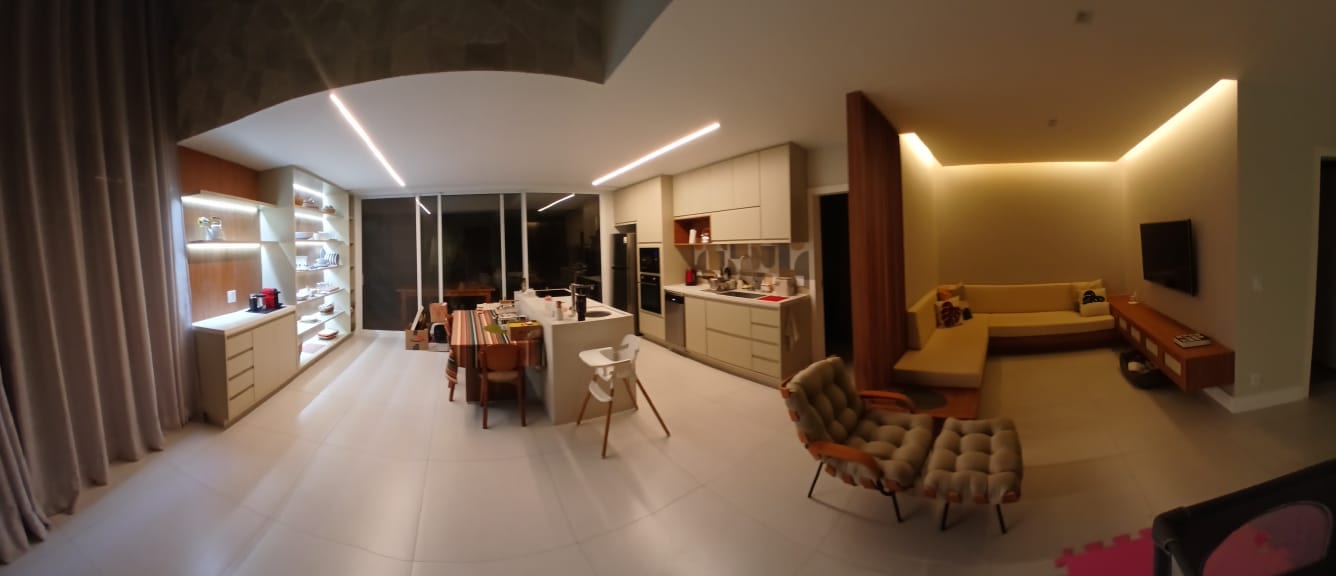 Sala de estar integrada à cozinha, com ilha, cristaleira iluminada e painel de TV em marcenaria planejada